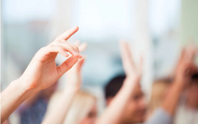Mehrere Personen heben die Hand bei einer Abstimmung.